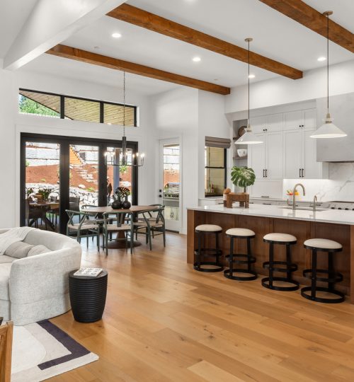 Beautiful living room and kitchen in new luxury home with white cabinets, wood beams, pendant lights and hardwood floors